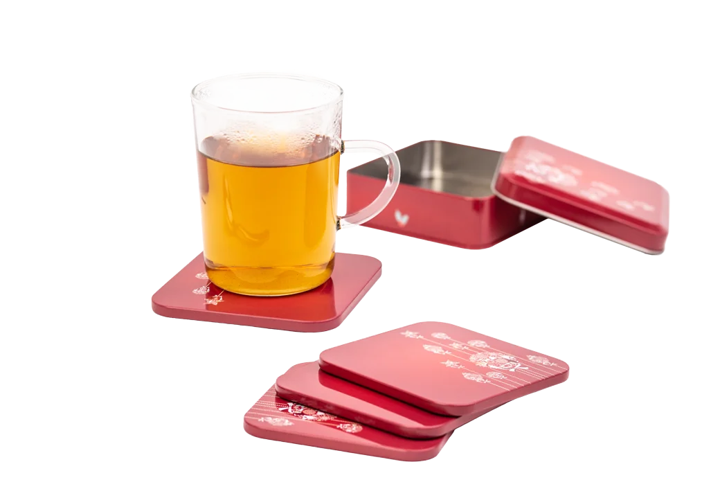 Rote Weihnachts-Untersetzer mit festlichem Weihnachtsmotiv, arrangiert auf einer dekorativen Oberfläche. Auf einem der Untersetzer steht ein Glas mit einem Getränk, während weitere Untersetzer daneben liegen.